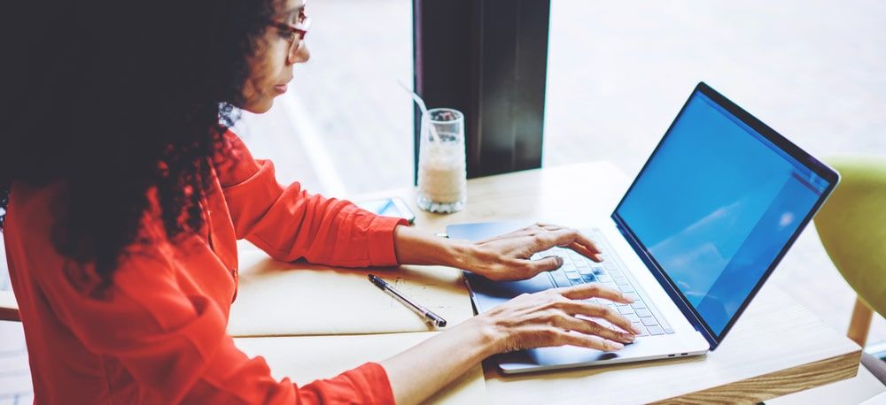 A woman with a red shirt writing on her laptop