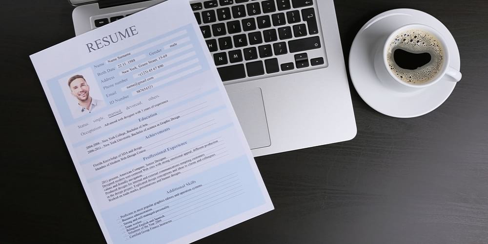 A laptopa on a table with a résumé on top and a black coffee on the right